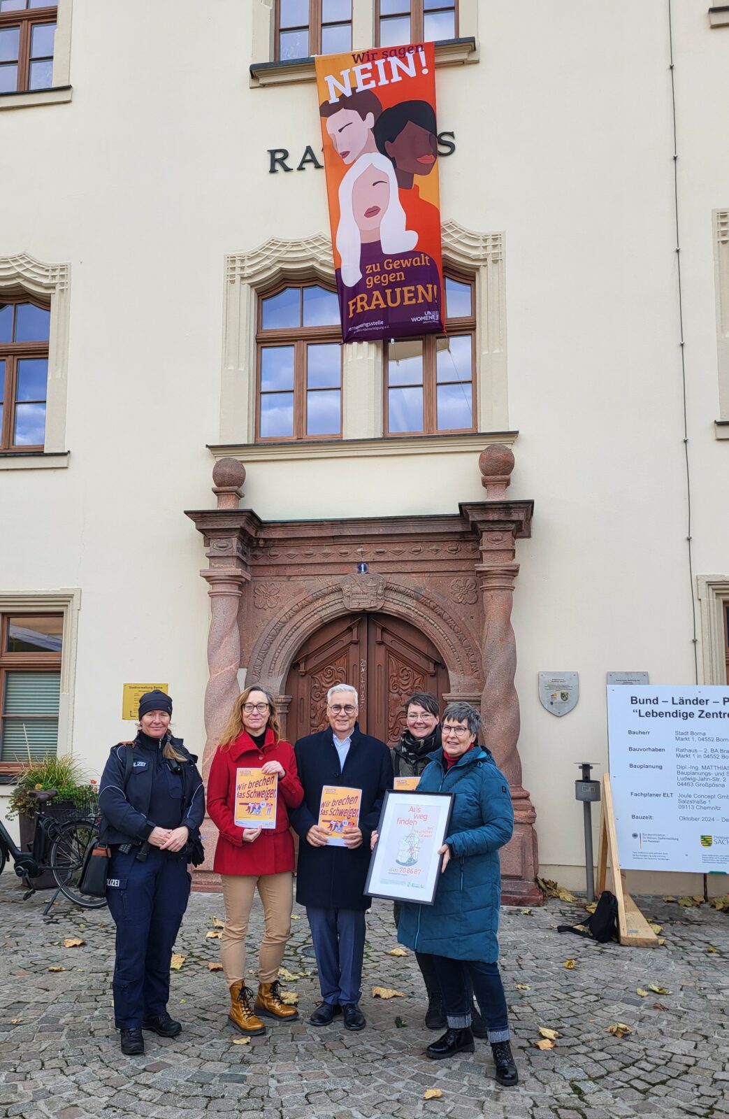 Fünf Personen stehen vor einem Plakat welches auf häusliche Gewalt aufmerksam macht 