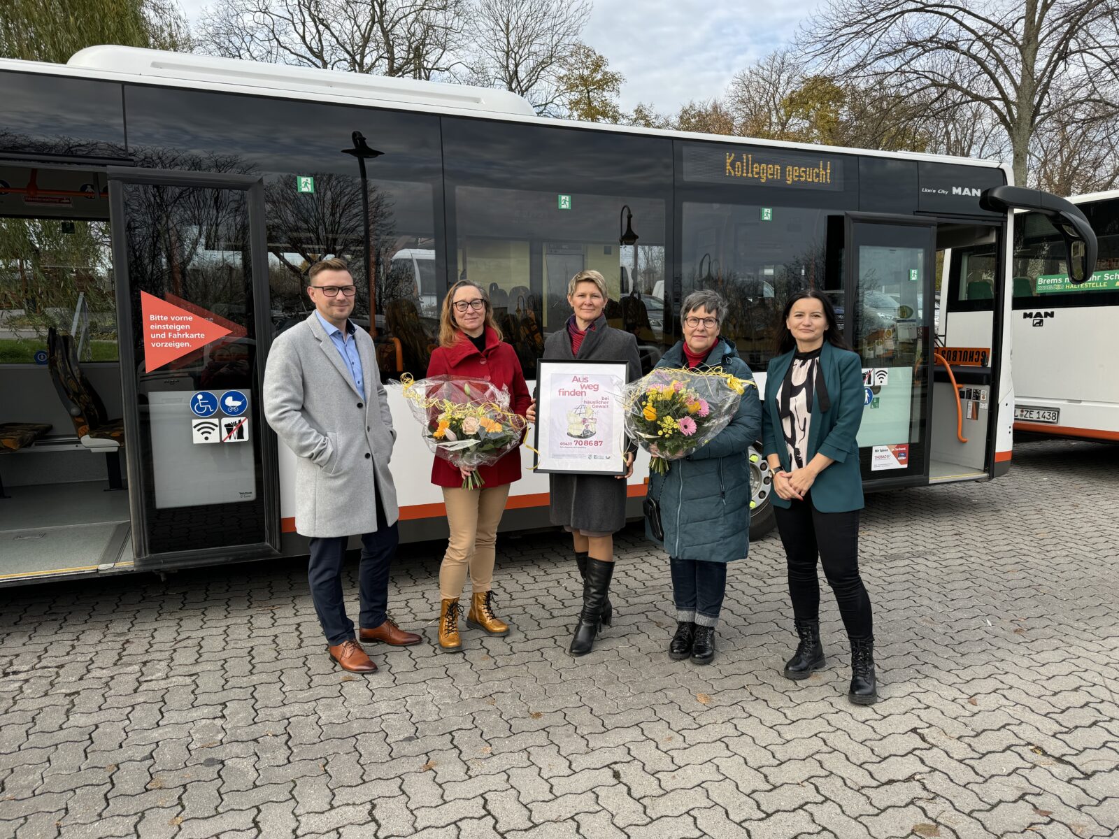 Fünf Personen stehen vor einem Bus mit einem Plakat