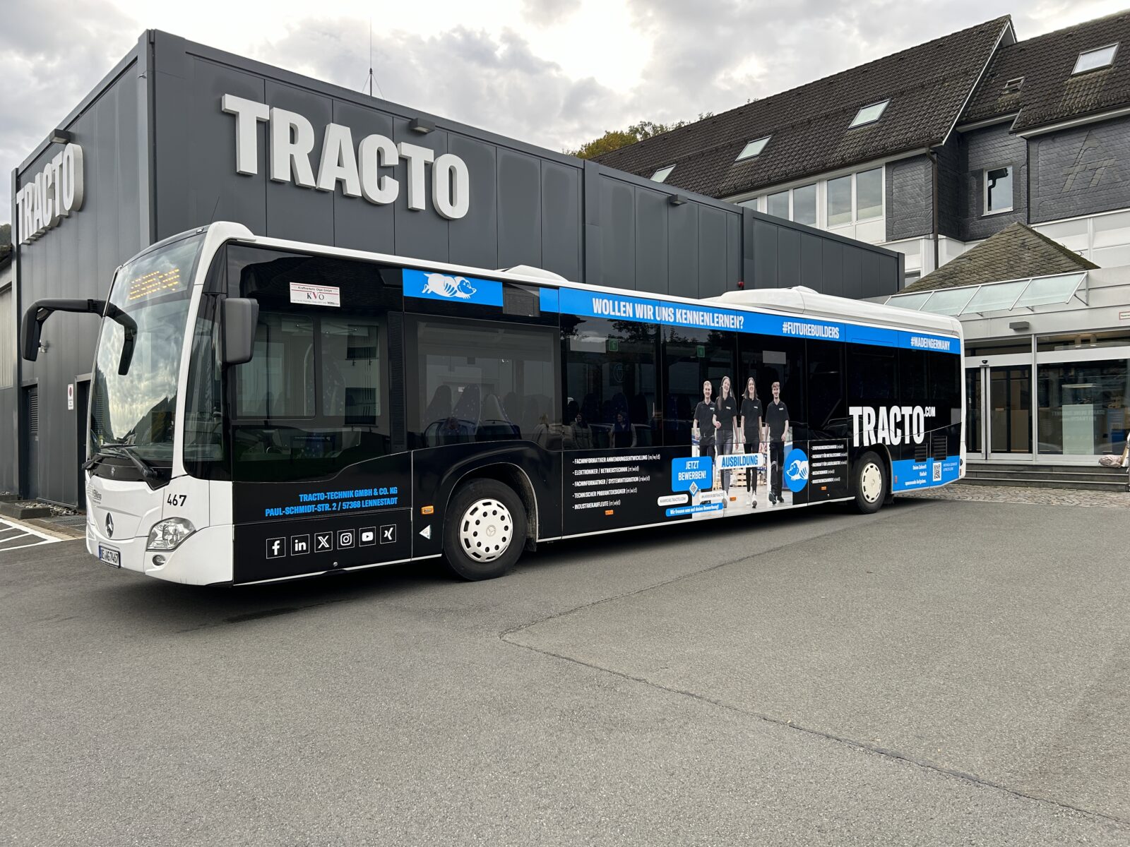 schwarz blauer Bus steht vor einem schwarzen Gebäude mit der Aufschrift Tracto