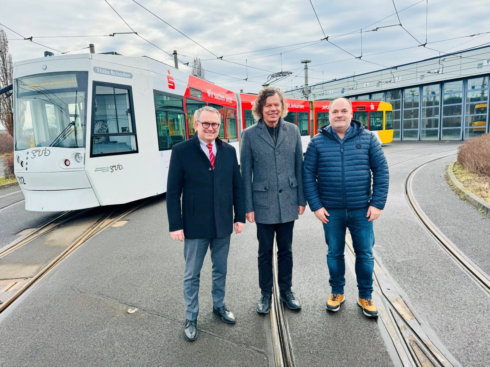 Drei Männer stehen vor einer Straßenbahn der Sparkasse 