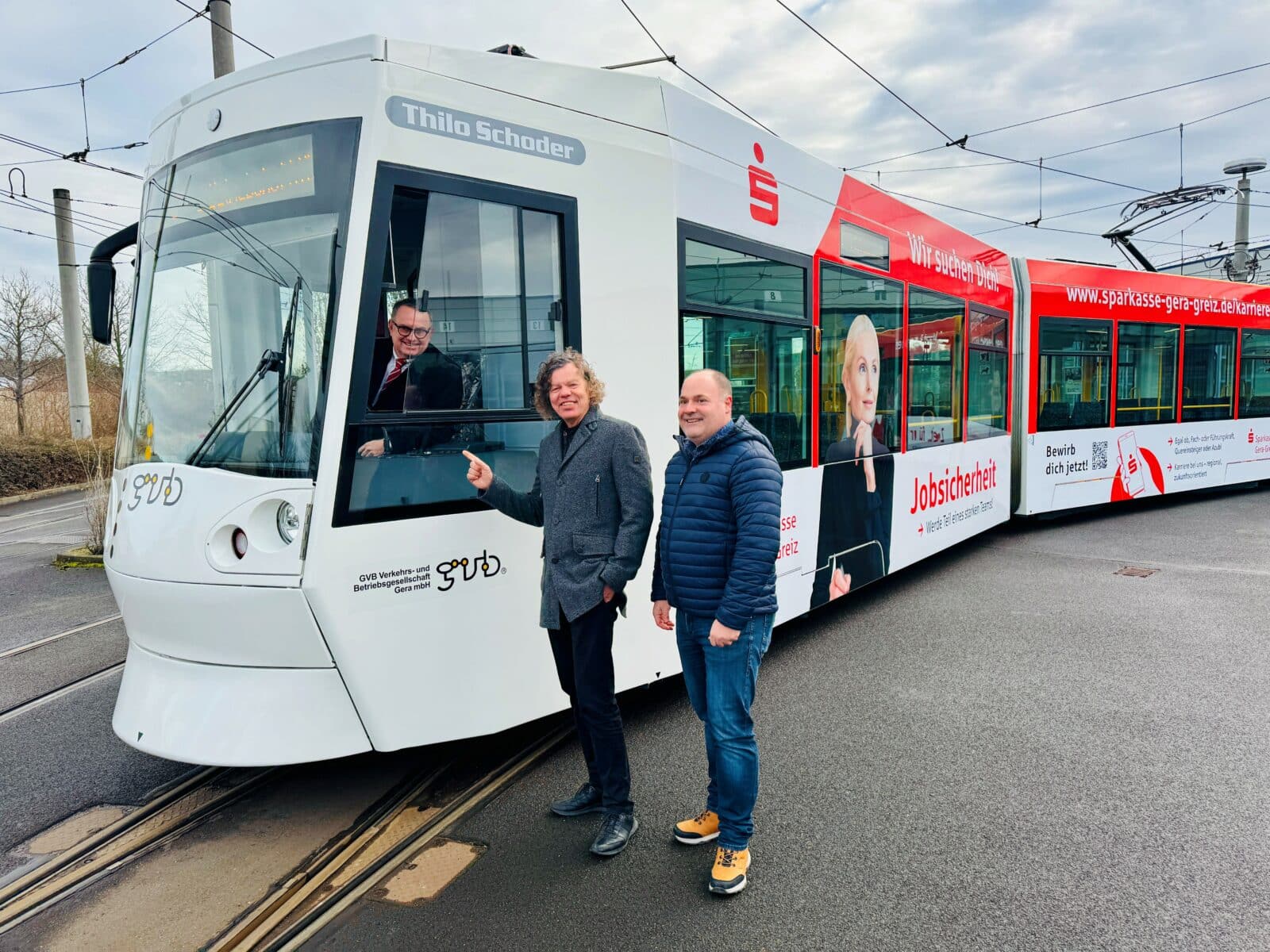 Zwei Männer stehen vor einer Straßenbahn und zeigen in die Fahrerkabine