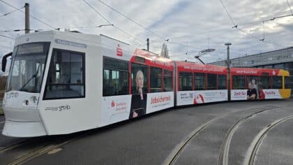 Seitenansicht einer weiß-roten Straßenbahn auf der großflächig Personen zu sehen sind